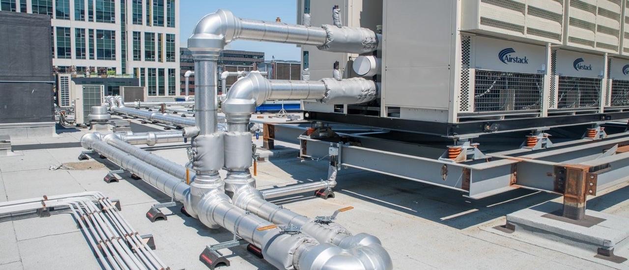 Multiple insulated pipe runs on rooftop supports beside plant